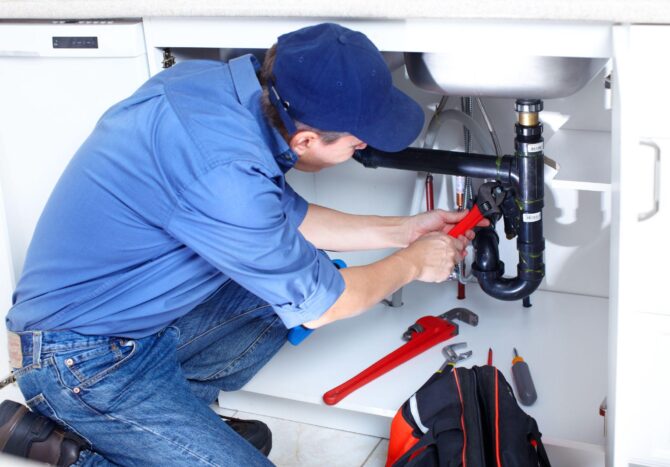 Plumber inspecting pipes under a sink — signs you need a plumber